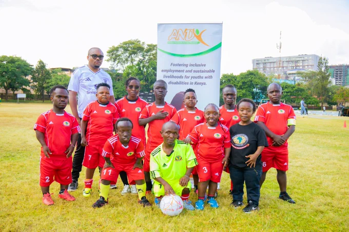 A group of 12 players wearing matching football uniforms on a grassy field posing confidently during an inclusive football tournament.