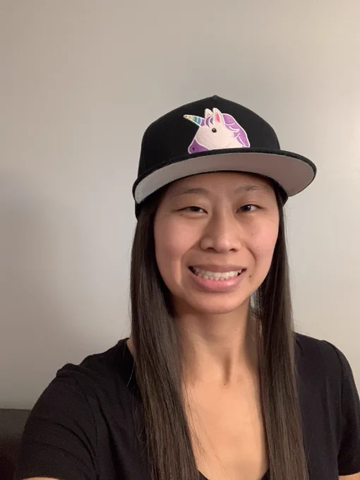 Mikaela smiling at the camera, in a black tshirt and wearing a black snapback hat with a unicorn on it.