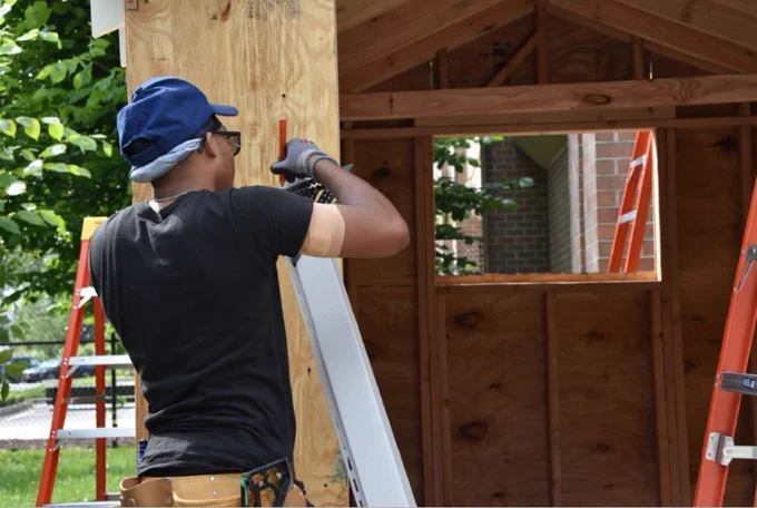 A construction academy participant marks a measurement while building a shed