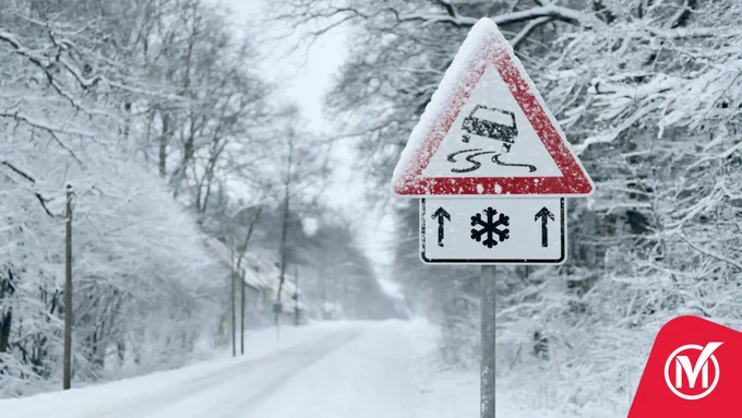 Snow-covered road with a slippery surface warning sign and a snowflake symbol indicating icy conditions ahead.