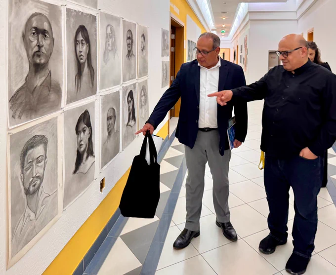 Arturo and Aissa deebi from the painting and printmaking program looking at student work in the corridors . The sketches show various faces with expressive, detailed features, creating a studious, creative atmosphere.
