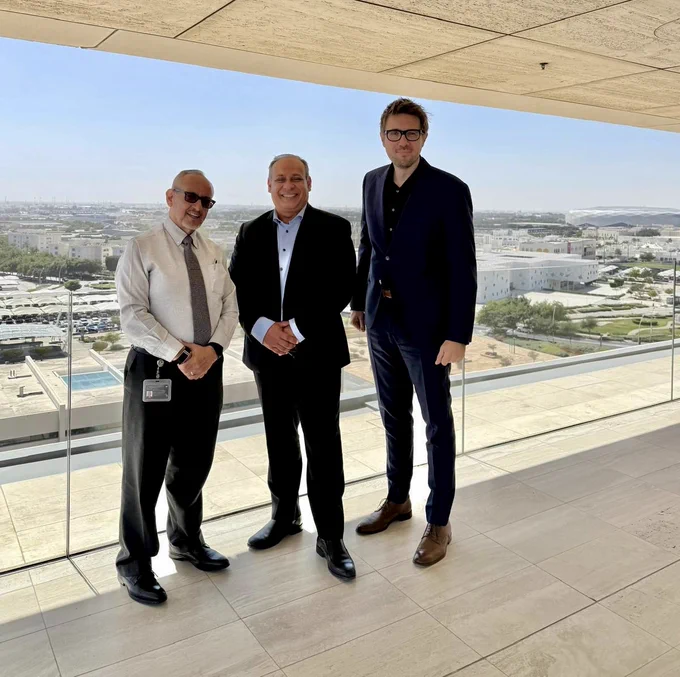 Francisco , Arturo , and Dean Amir at the Qatar Foundation headquarters . Behind them is a sprawling bird's-eye view of a modern city landscape under a clear, bright sky.