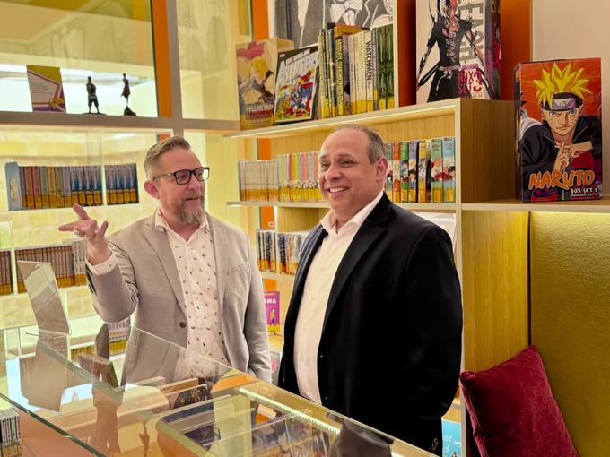 Mike Wirtz from the Comics Lab with Arturo . Behind them, wooden shelves are packed with manga and graphic novels, including a prominent Naruto box set and Fullmetal Alchemist volumes.