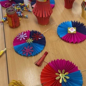 A selection of crafts for Chinese New Year, including pink, blue and gold folded paper fan decorations and red and gold paper lanterns