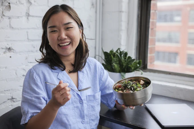 Someone smiles while holding a fork and a reusable silver bowl.