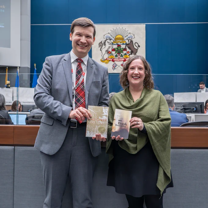 Photo of two individuals smiling and holding a book.