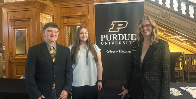 Male and female students standing with female professor and Purdue College of Education banner at Indiana Statehouse
