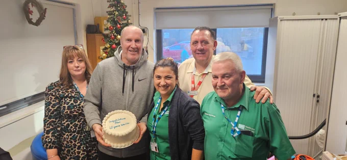 A group of five people smiling indoors, one person holding a cake