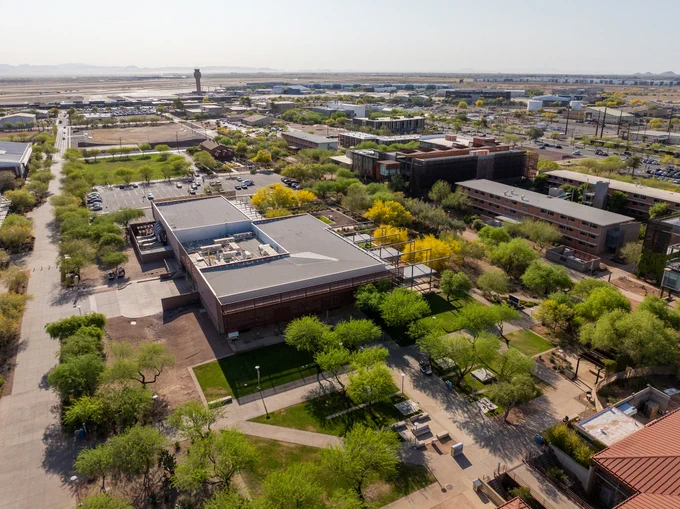 Aerial view of a sprawling campus with multiple buildings surrounded by green trees and pathways under a clear sky.