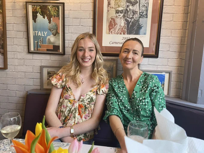 Holly and her mum inside a restaurant with Italian wall art behind them.