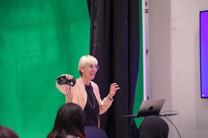 Sabine Schrunder giving a demonstration at the studio . She is holding a camera flash . A laptop is in front of her and students are in the foreground