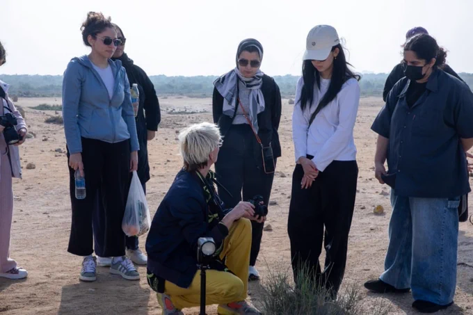 Sabine with students in the desert . She is holding a camera while another is on a tripod in front of her