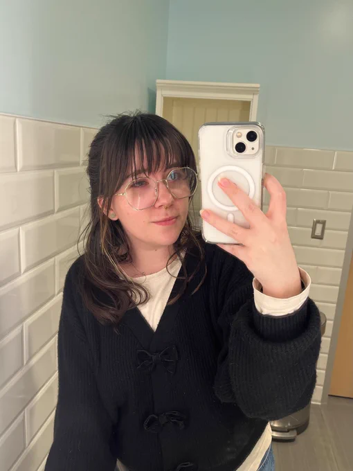 a mirror selfie of me. i’m wearing a black cardigan over an off white shirt. my brown hair is collar bone length. my bangs referenced in the post are falling just below my eyebrows