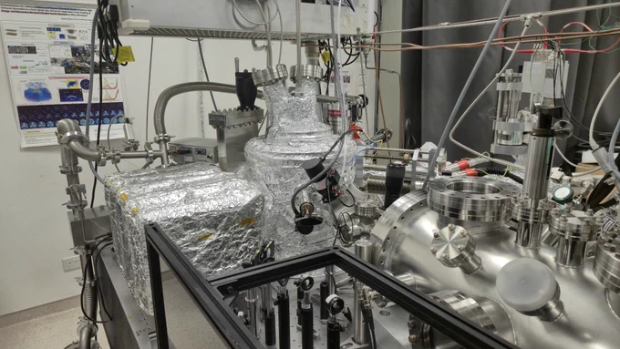 Laboratory setup with a complex semiconductor imaging system, featuring stainless steel vacuum chambers, foil-wrapped components, valves, cables, and optical mounts used for ultra-fast electron dynamics experiments.