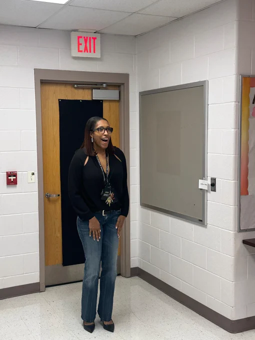 Rhoshanda Pyles, principal of Rockville High School, standing in a hallway near a wooden door with an illuminated red exit sign above it.