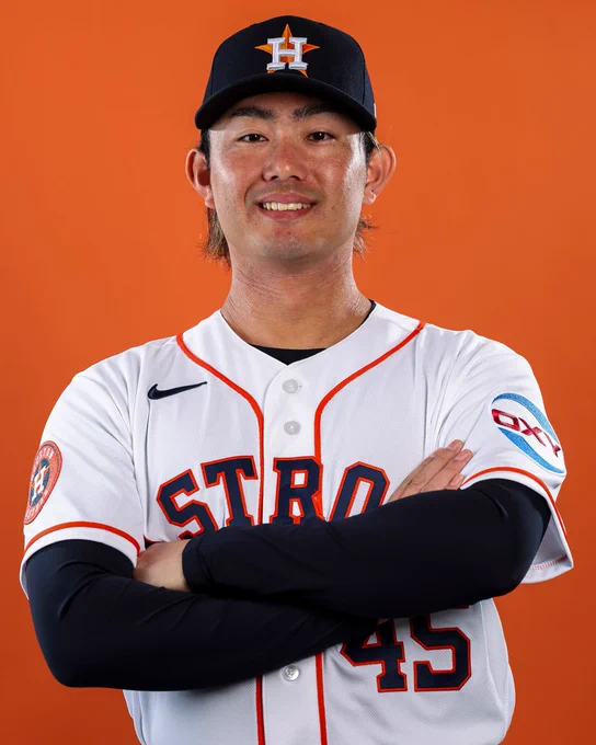 Tatsuya Imai smiles for a posed photo with his arms crossed in a white Houston Astros jersey with navy lettering, orange trim and a navy Houston Astros cap.