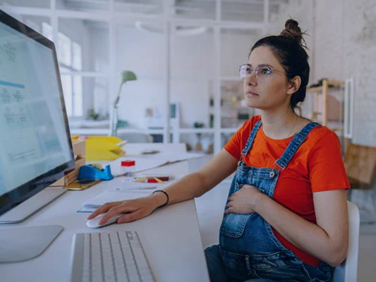 Pregnant woman working at a desktop computer in an office setting