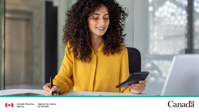 A smiling person looks down at a calculator and is writing something down.