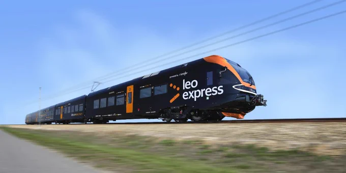 A sleek black train with orange accents travels swiftly on tracks. The train features the logo "Leo Express" prominently on its side. The setting is outdoors with a clear blue sky.
