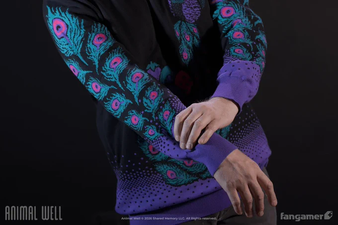 A photo of a model wearing the Peacock's Treasure sweater, focused on the feather motif on the sleeves. It's a black knit sweater with a dithered purple gradient at the waist and the cuffs and a pink, turquoise, and purple peacock design on the chest and sleeves.