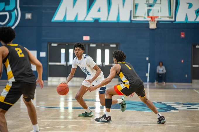Basketball player in white dribbling the ball while guarded closely by a defender in black and yellow on an indoor court.