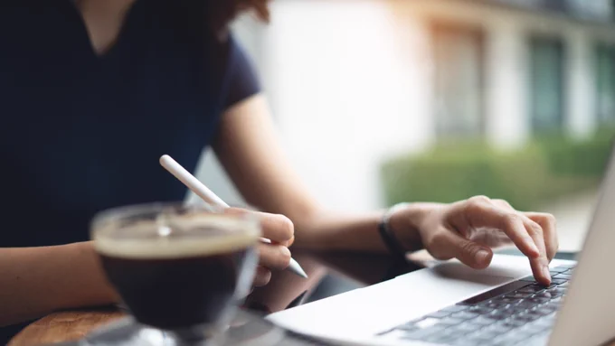Image of a person enrolling in auto debit on their phone or laptop in a coffee shop.  