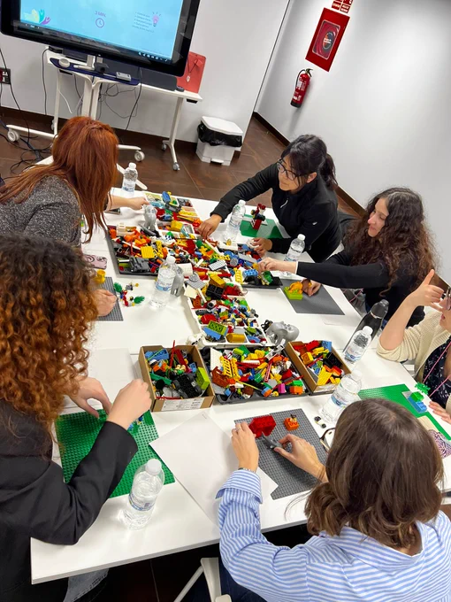 Plano general de la mesa con las piezas de lego, al rededor están las alumnas cogiendo piezas para colocar en su tapete.