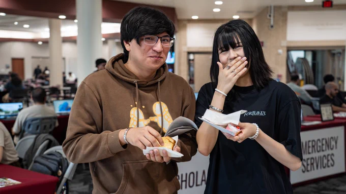Two students smiling for the camera as they hold their sweet bread.