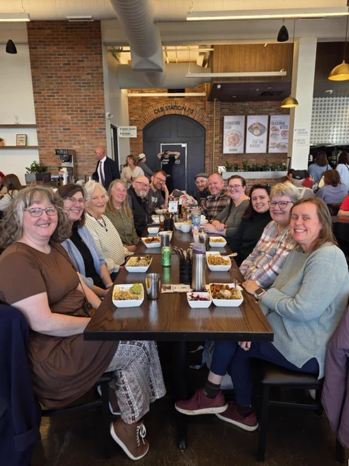 Photo shows a group of women and men sitting at a long table stretching away from the photographer.