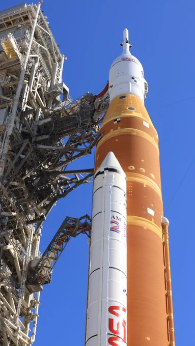 A side view shows one of the twin SLS (Space Launch System) solid rocket boosters, core stage, and the Orion spacecraft with its launch abort system at Launch Complex 39B at NASA\u2019s Kennedy Space Center in Florida on Tuesday, Feb. 10, 2026. The orange core stage of the Artemis II rocket stands between two white solid rocket boosters and is topped with the white Orion spacecraft. To the left of the rocket stands the trussed structure of the mobile launcher. The sky is blue in the background. Credit: NASA/Ben Smegelsky
