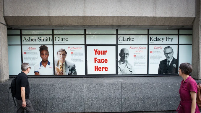 The windows of the King's building on the Strand covered with images of famous King's alumni. People are walking past and looking at the windows.