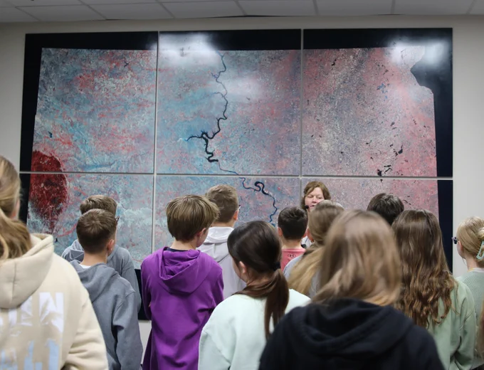 Group of students attentively observing a large multi-panel satellite map displayed on a wall.
