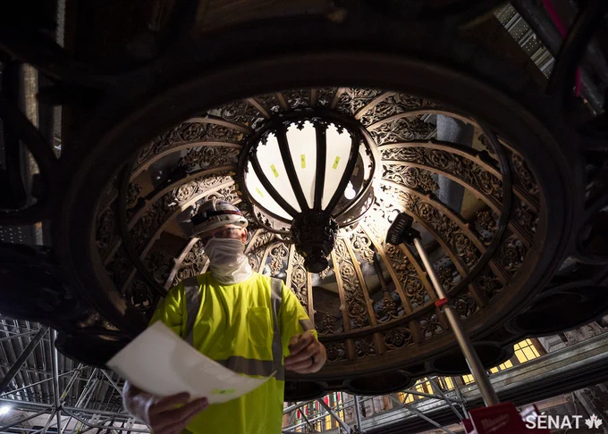 Un travailleur se tient sous un lustre à l’intérieur de la Chambre du Sénat de l’édifice du Centre.