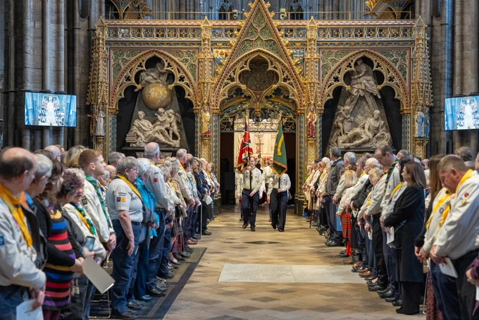 A group of Scouts carrying flags in procession through Westminster Abbey, with members of the congregation standing on either side