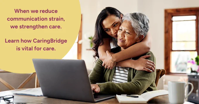 Adult daughter hugging elderly woman sitting at a table with a laptop, symbolizing support and care.
