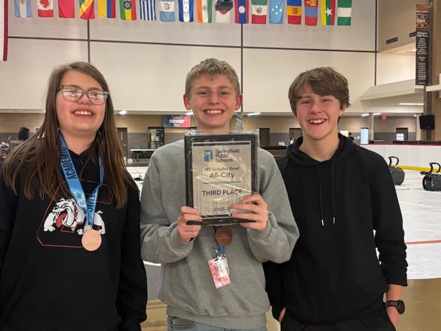 Three students holding a plaque with one student wearing a medal