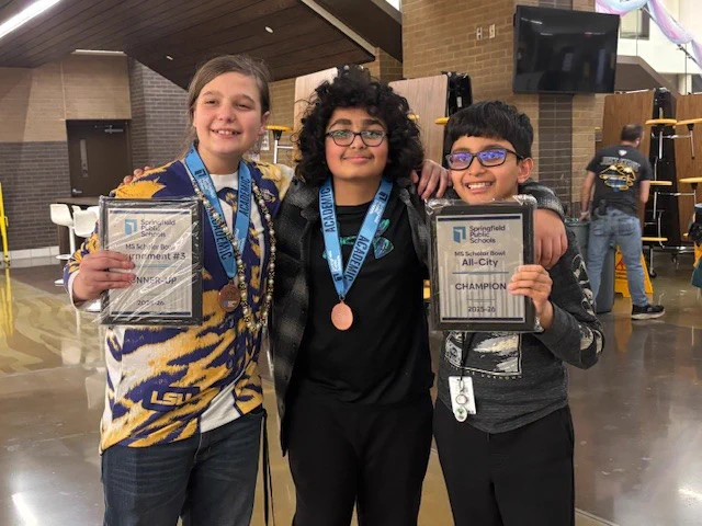 Three students wearing medals and holding two plaques