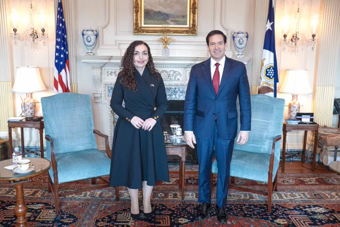 Secretary Rubio stands next to Kosovo President Osmani in Washington, DC on February 20, 2026. They stand in front of two arm chairs and a coffee table. A fireplace is seen behind the officials with vases on the mantle, U.S. and Department of State flags displayed on either side of the fireplace, and a framed painting above the mantle. (State Department/Freddie Everett)