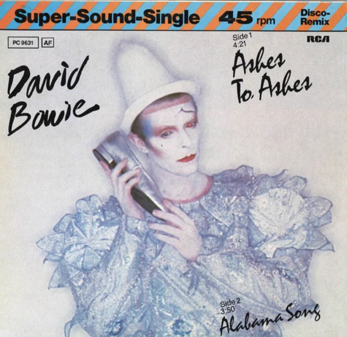 45 rpm single record cover of David Bowie's Ashes to Ashes, showing Bowie in an amorphous blouse and a white cone shaped Pierrot hat with clown makeup holding a silver shoe to the side of his facec like a telephone