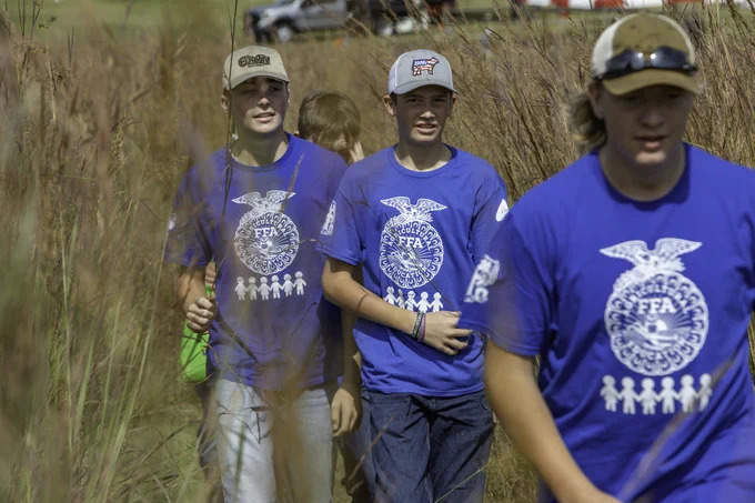 A group of FFA members wearing blue t-shirts with the FFA emblem walk through a field at Farm Science Review.