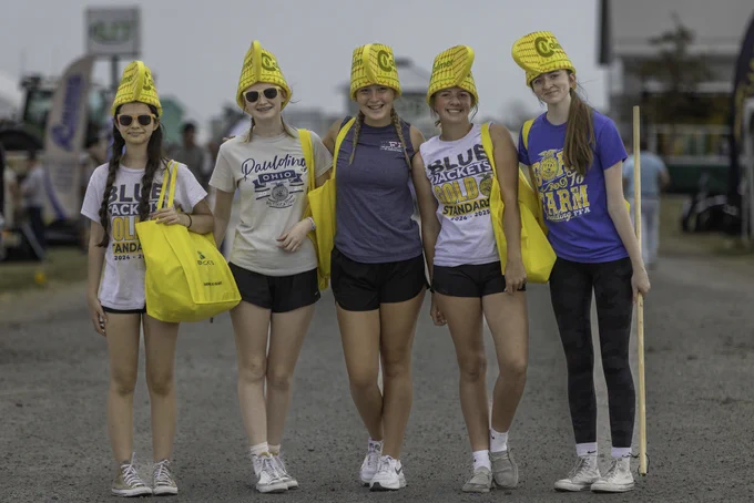 A group of FFA members wearing FFA chapter t-shirts and hats shaped like ears of corn smile for a picture.