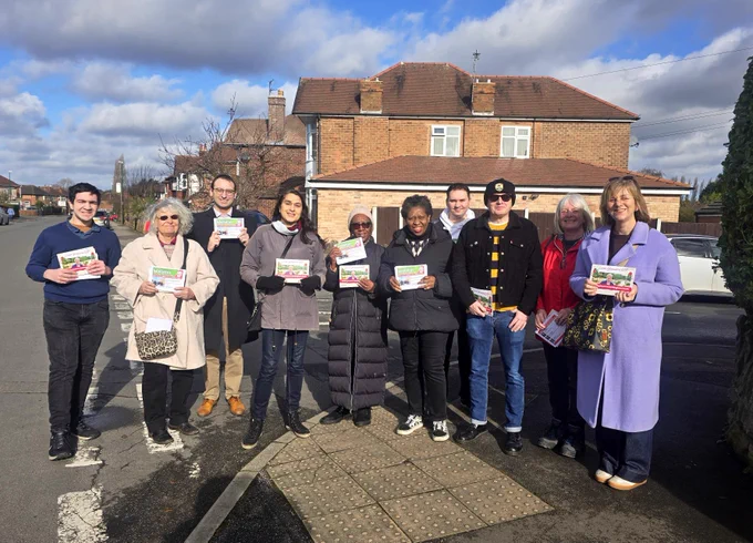 A big group of Labour councillors and volunteers standing on Woodhall Road, in the sunshine holding leaflets