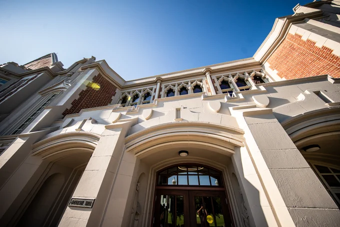 Exterior of Jones Family Welcome Center at Jacobson Hall at the University of Oklahoma, showcasing its brick and stone facade with arched windows and decorative architectural details against a clear blue sky.