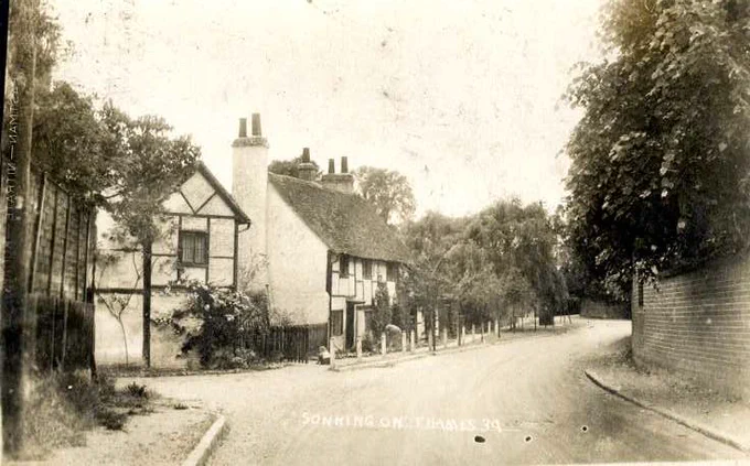 A black and white photo of an empty road in Sonning, there are houses to the left and a wall to the right.