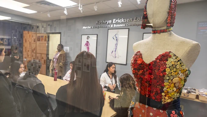 a group of students sit in the merchandising lab with a button dress on a mannequin in the foreground