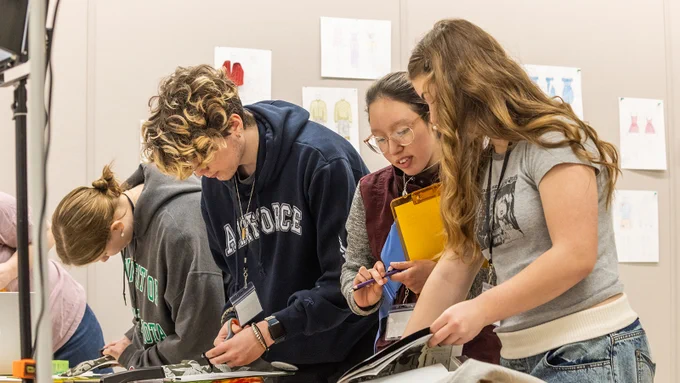 three students work on an activity during a TMFD Expo session while a teacher provides assistance