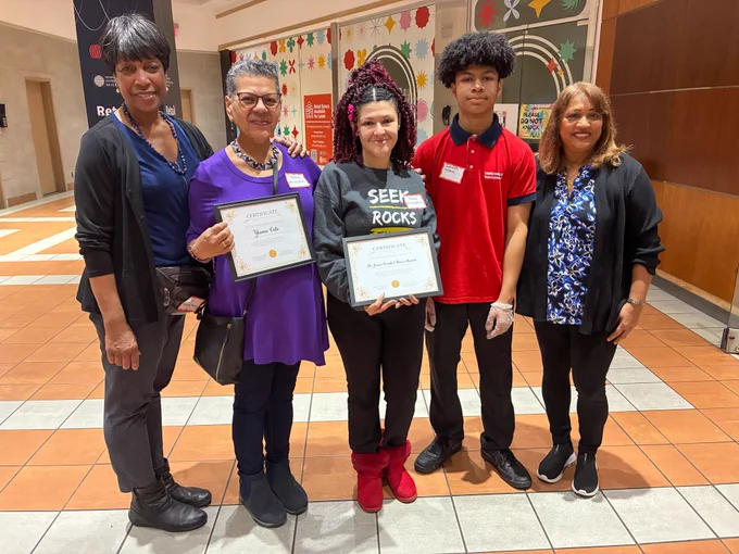 Group photo of five people, two of whom hold framed certificates of appreciation. 