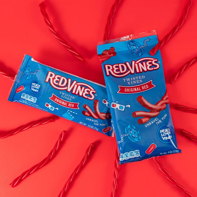 Two packages of Red Vines Twisted Vines Original Red licorice are displayed against a vibrant red background, surrounded by individual licorice pieces.