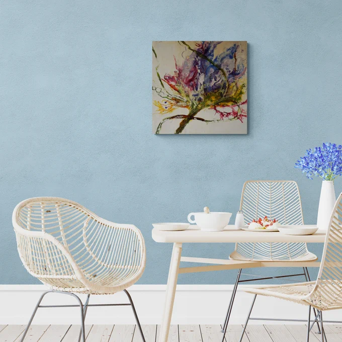 A calm, light-blue dining space with rattan chairs and a minimalist wooden table. The vibrant abstract encaustic painting hangs centered on the wall, its organic purple, green, and yellow forms standing out against the soft pastel room.