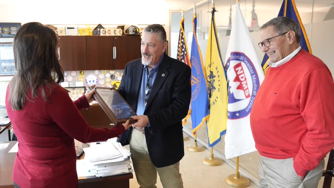 Amy Mouro of the DC Fire and EMS Foundation handing a plaque and commemorative challenge coins from the DC Fire and EMS Foundation and the Families of Flight 5342 to Jon Greene, ASPR Deputy Assistant Secretary for Response.